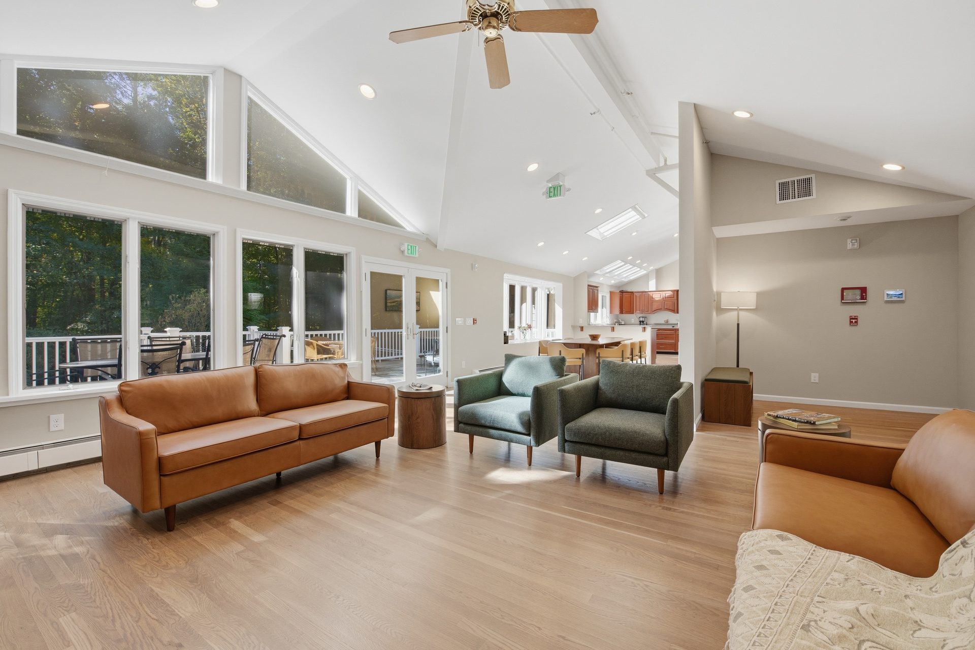 Great room with vaulted white ceilings, light wood floors, leather sofas and green armchairs, opening to the kitchen