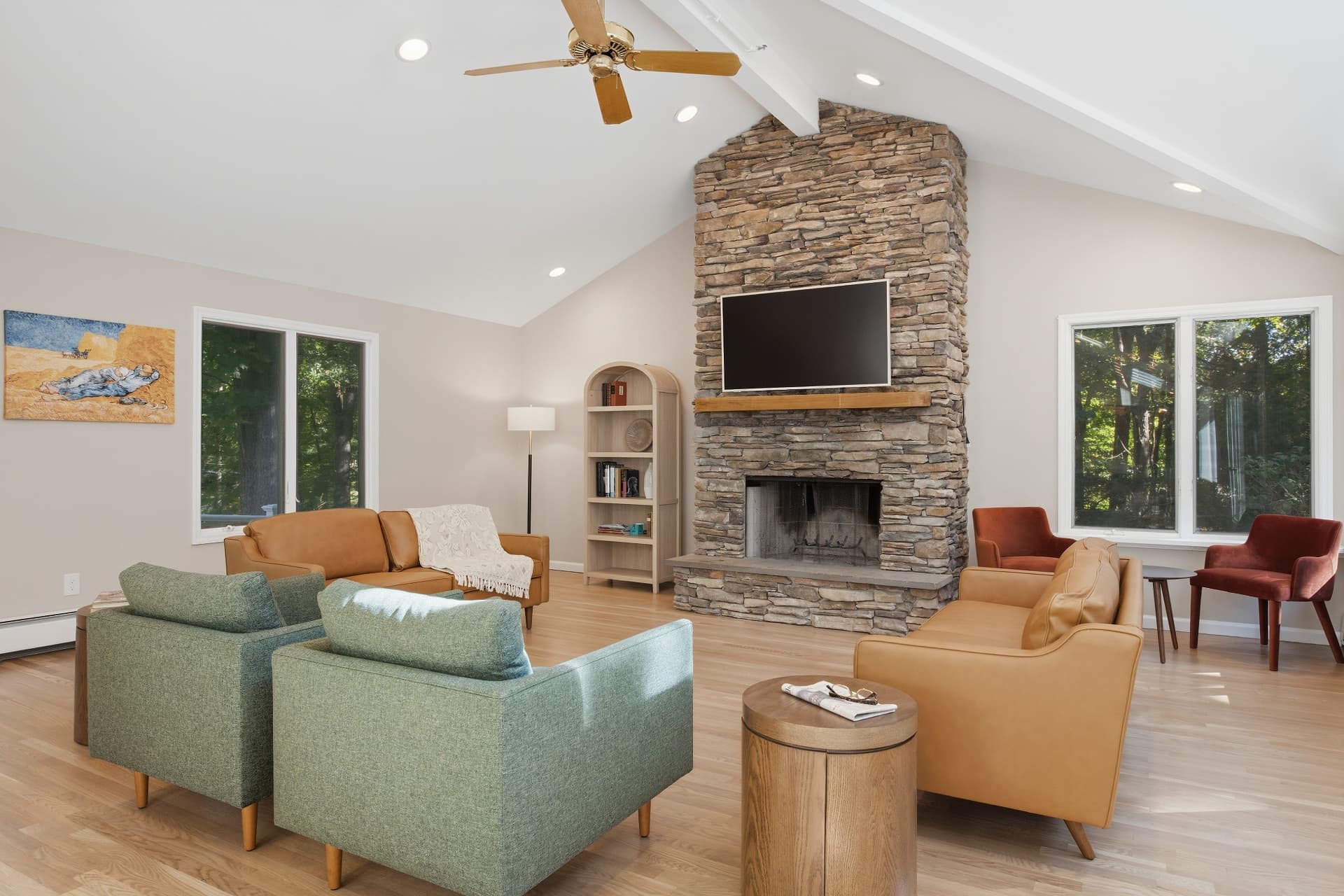 Great room with a tall stacked-stone fireplace, vaulted ceilings and warm leather and green seating
