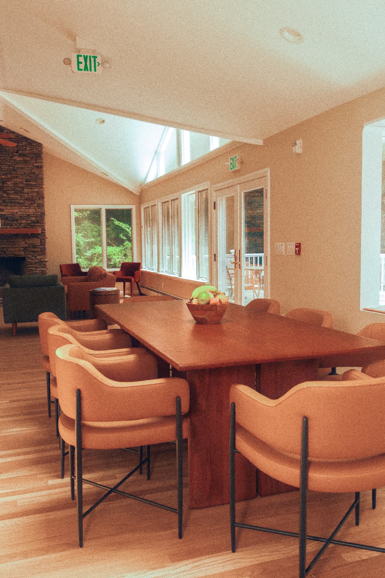 Long wooden dining table with a bowl of fruit beside the sunlit great room