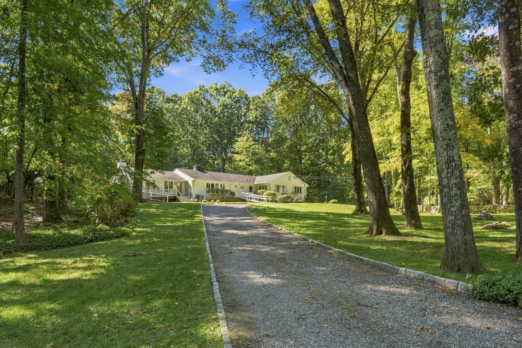 The Fox Hill Road home seen up a long gravel driveway edged with stone, between a green lawn and tall mature trees