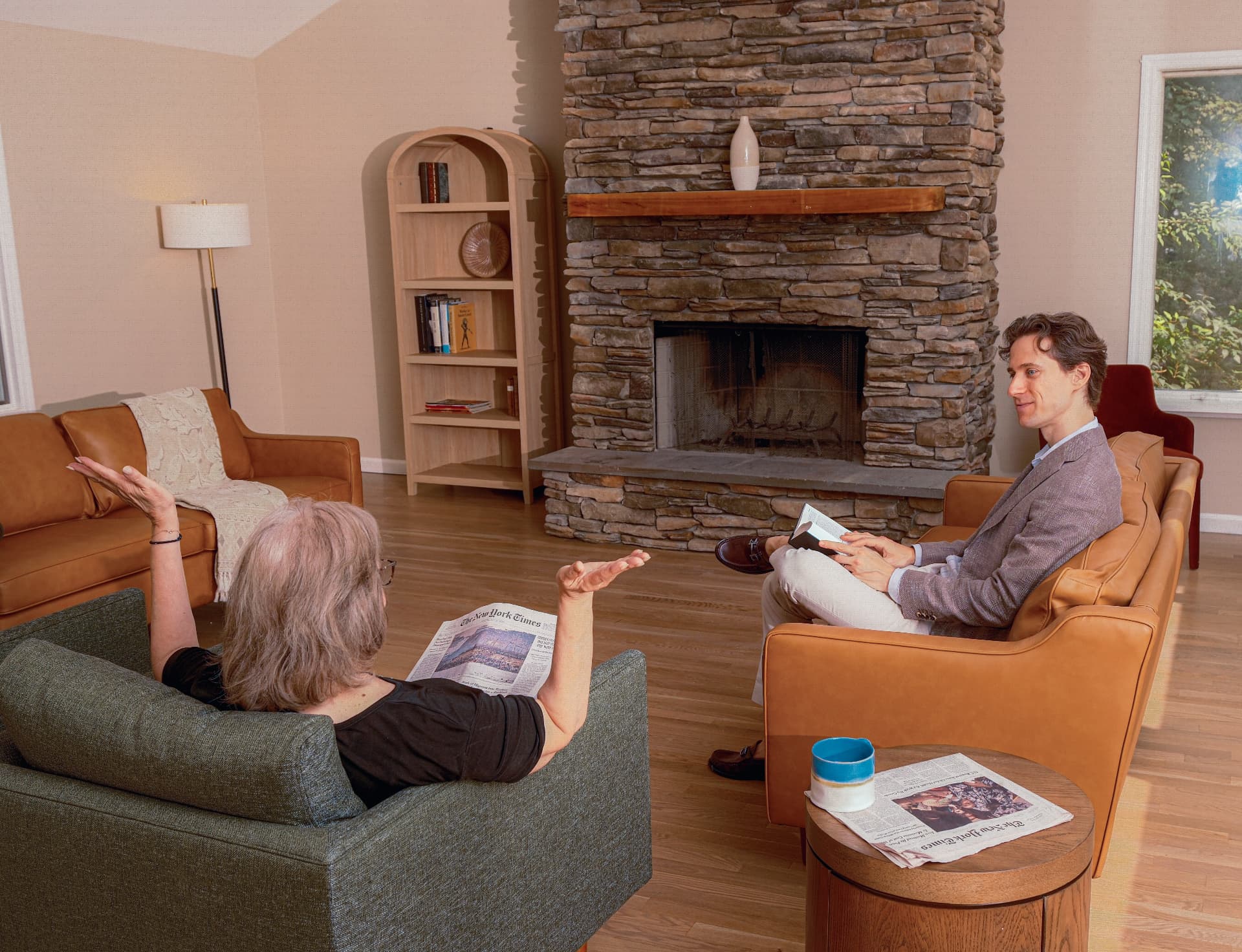 A resident and a member of the Sycamore Collection team talking beside the stone fireplace in the living room.